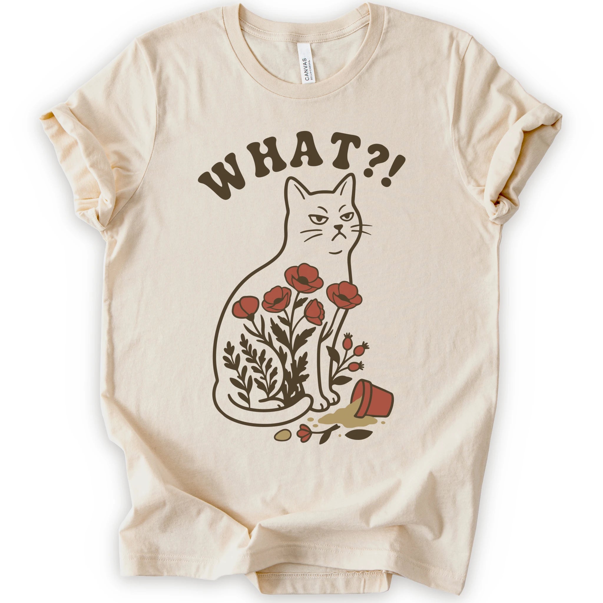 Natural graphic t-shirt with “WHAT?!” text above an unimpressed cream cat with red flowers beside a knocked-over plant pot