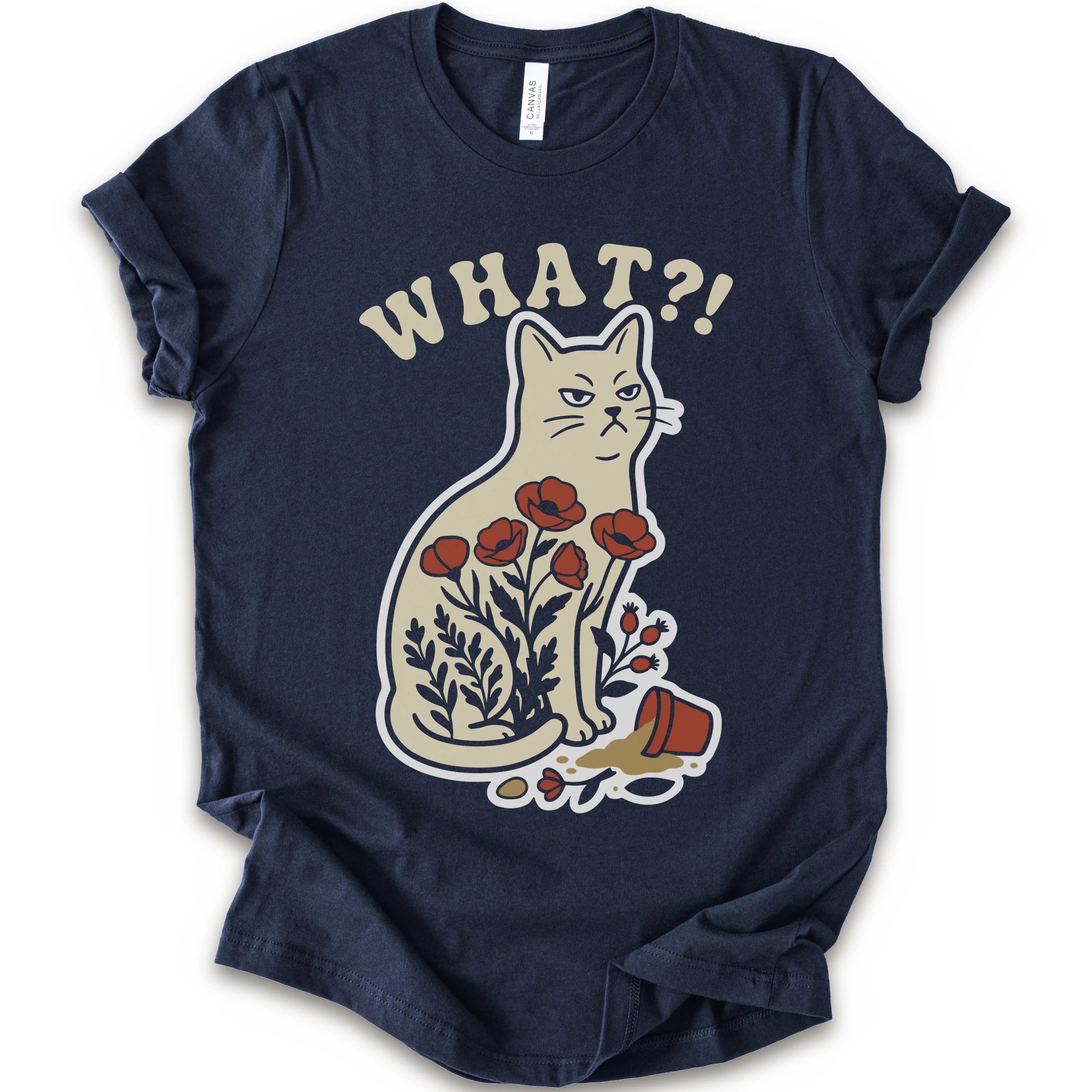 Navy graphic t-shirt with “WHAT?!” text above an unimpressed cream cat with red flowers beside a knocked-over plant pot