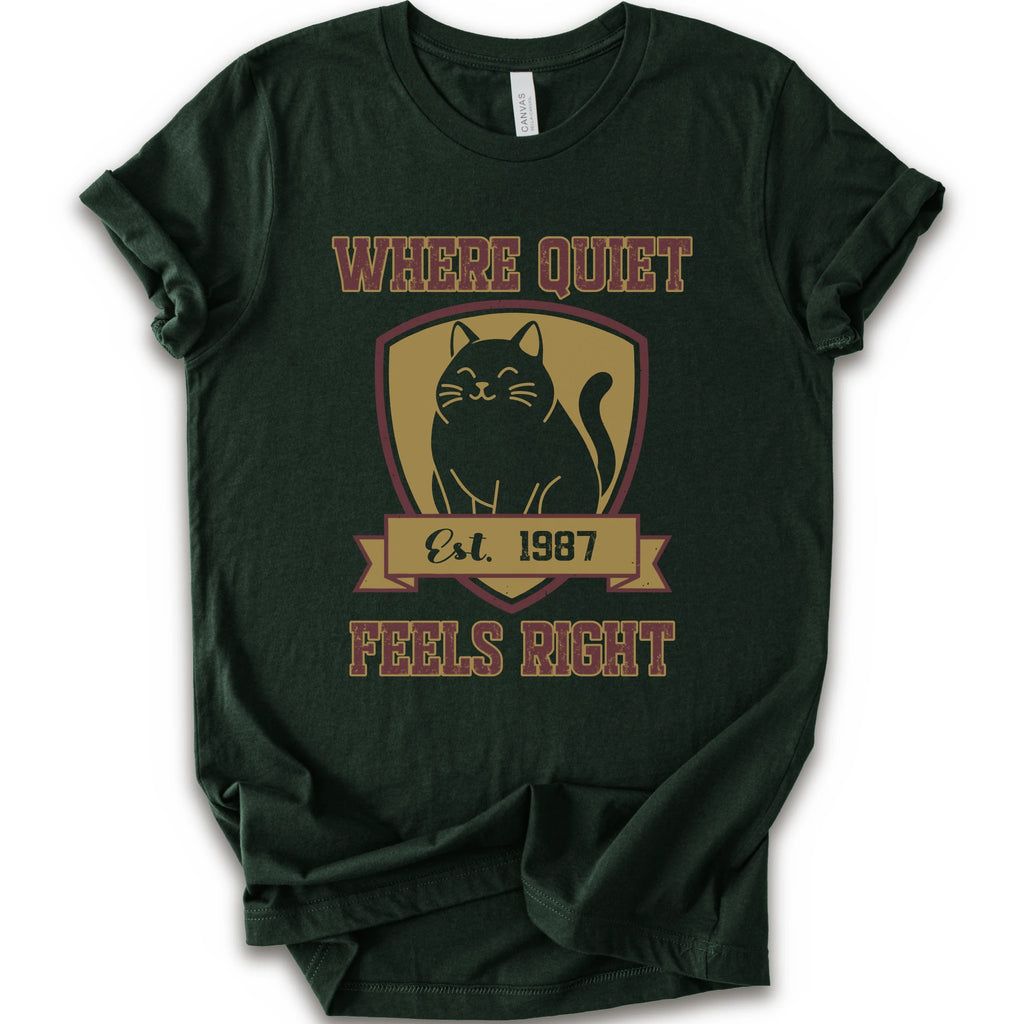 A forest short-sleeve t-shirt with a vintage-style graphic on the front featuring a black cat inside a gold shield and the text 'WHERE QUIET FEELS RIGHT Est. 1987'.