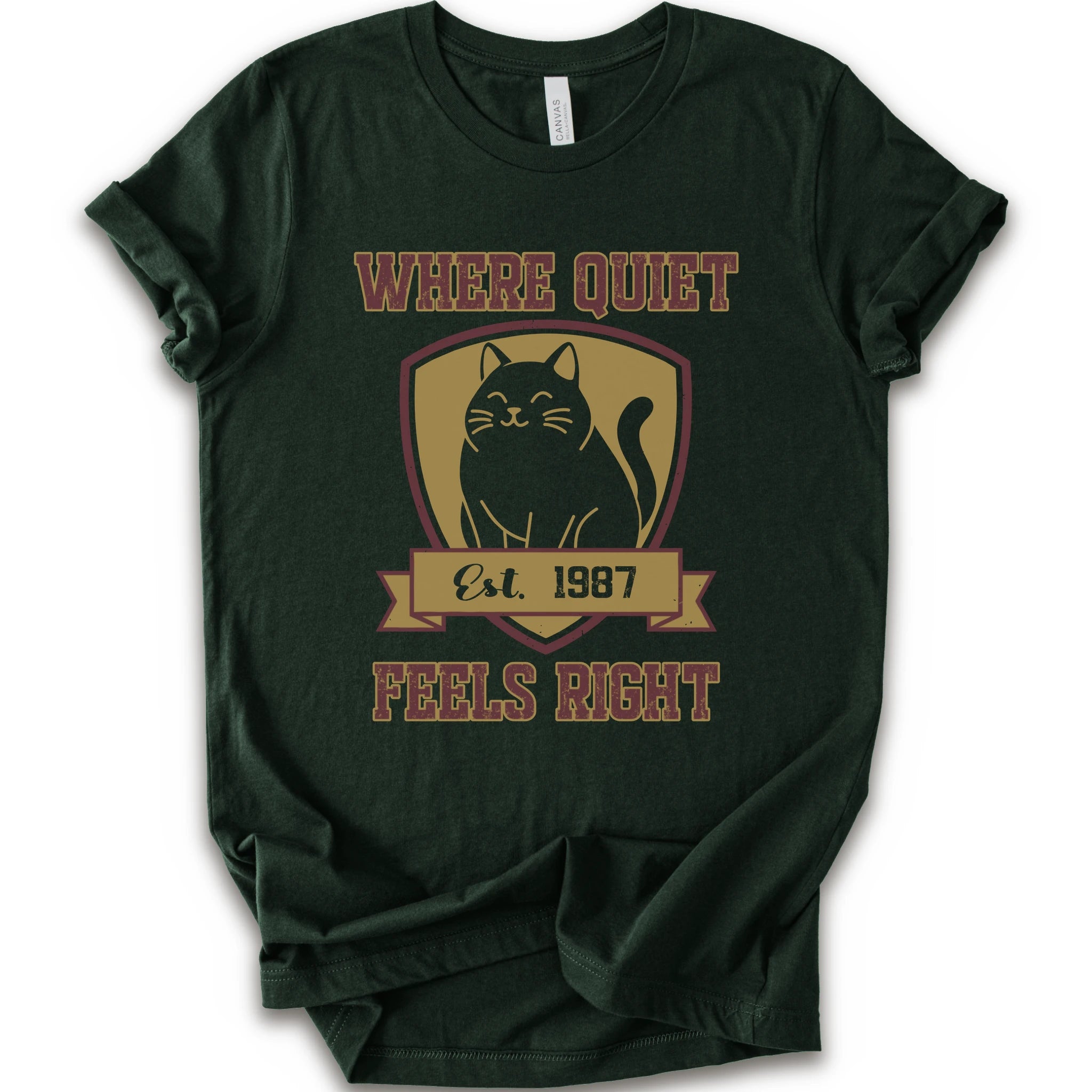 A forest short-sleeve t-shirt with a vintage-style graphic on the front featuring a black cat inside a gold shield and the text 'WHERE QUIET FEELS RIGHT Est. 1987'.