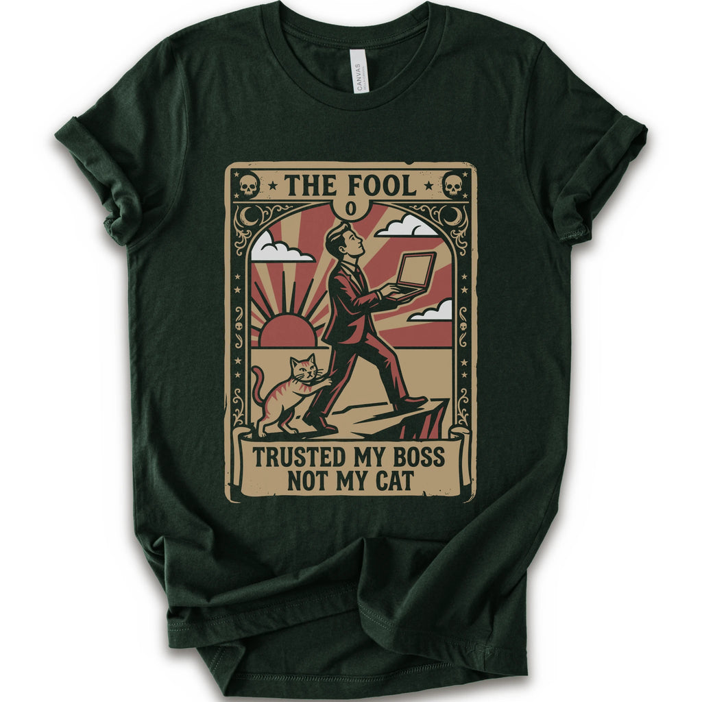 A forest short-sleeve crewneck t-shirt with a vintage-style graphic print on the front. The graphic is styled like an old tarot card, featuring a man in a suit walking on a cliff while a cat watches, with the text 'THE FOOL' at the top and 'TRUSTED MY BOSS NOT MY CAT' at the bottom.