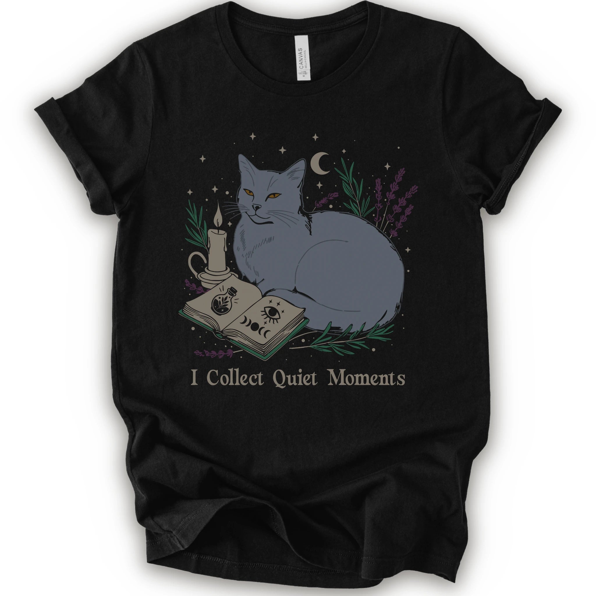 A black short-sleeve crewneck t-shirt featuring a graphic of a gray cat lying next to an open book, a candle, and lavender under a crescent moon, with the text 'I Collect Quiet Moments' printed below.