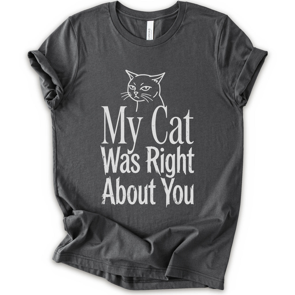 A asphalt short-sleeve crewneck T-shirt with a cat rendered in white outline sits above the text “My Cat Was Right About You,” arranged in oversized mixed serif and distressed lettering.