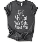 A asphalt short-sleeve crewneck T-shirt with a cat rendered in white outline sits above the text “My Cat Was Right About You,” arranged in oversized mixed serif and distressed lettering.