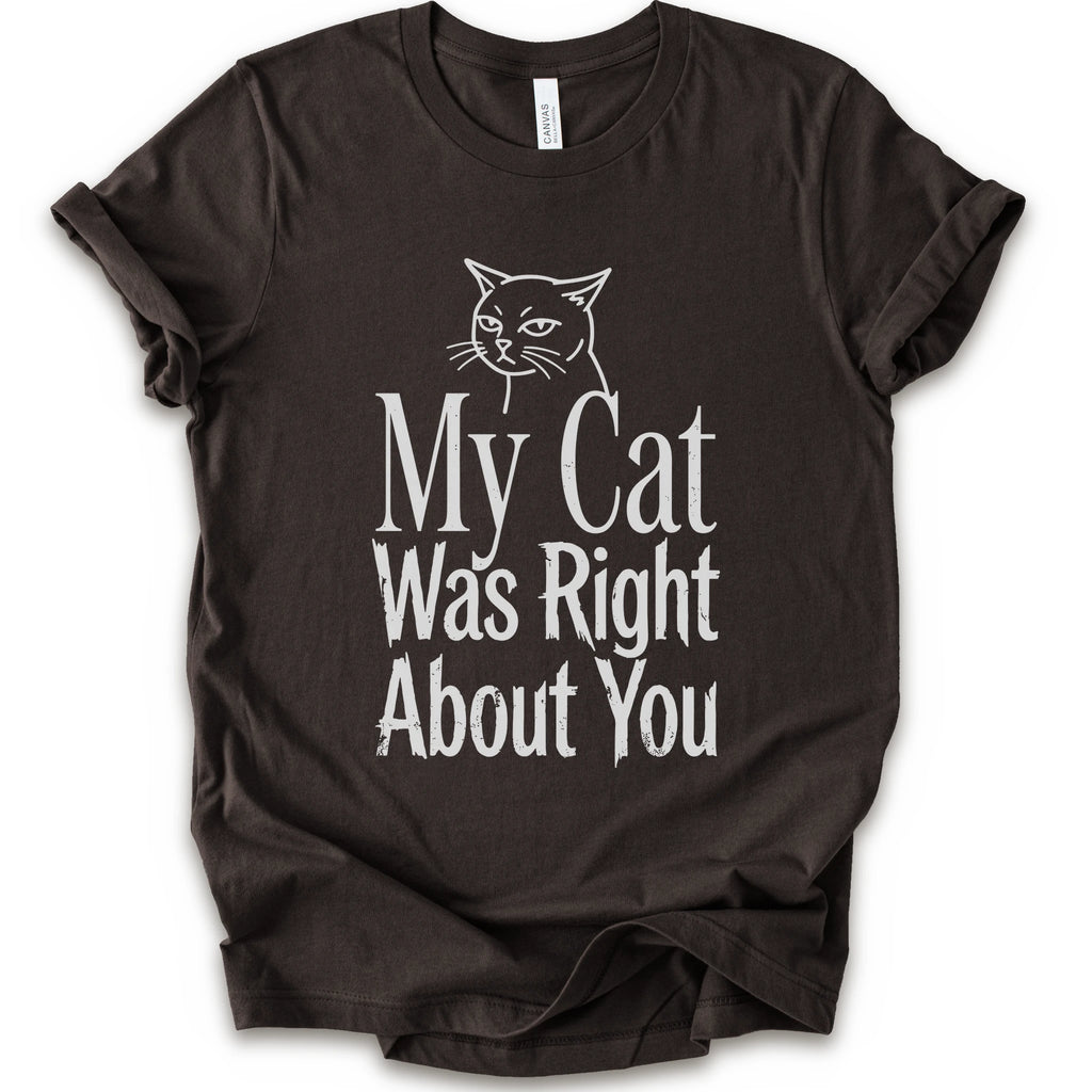 A brown short-sleeve crewneck T-shirt with a cat rendered in white outline sits above the text “My Cat Was Right About You,” arranged in oversized mixed serif and distressed lettering.