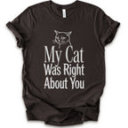 A brown short-sleeve crewneck T-shirt with a cat rendered in white outline sits above the text “My Cat Was Right About You,” arranged in oversized mixed serif and distressed lettering.