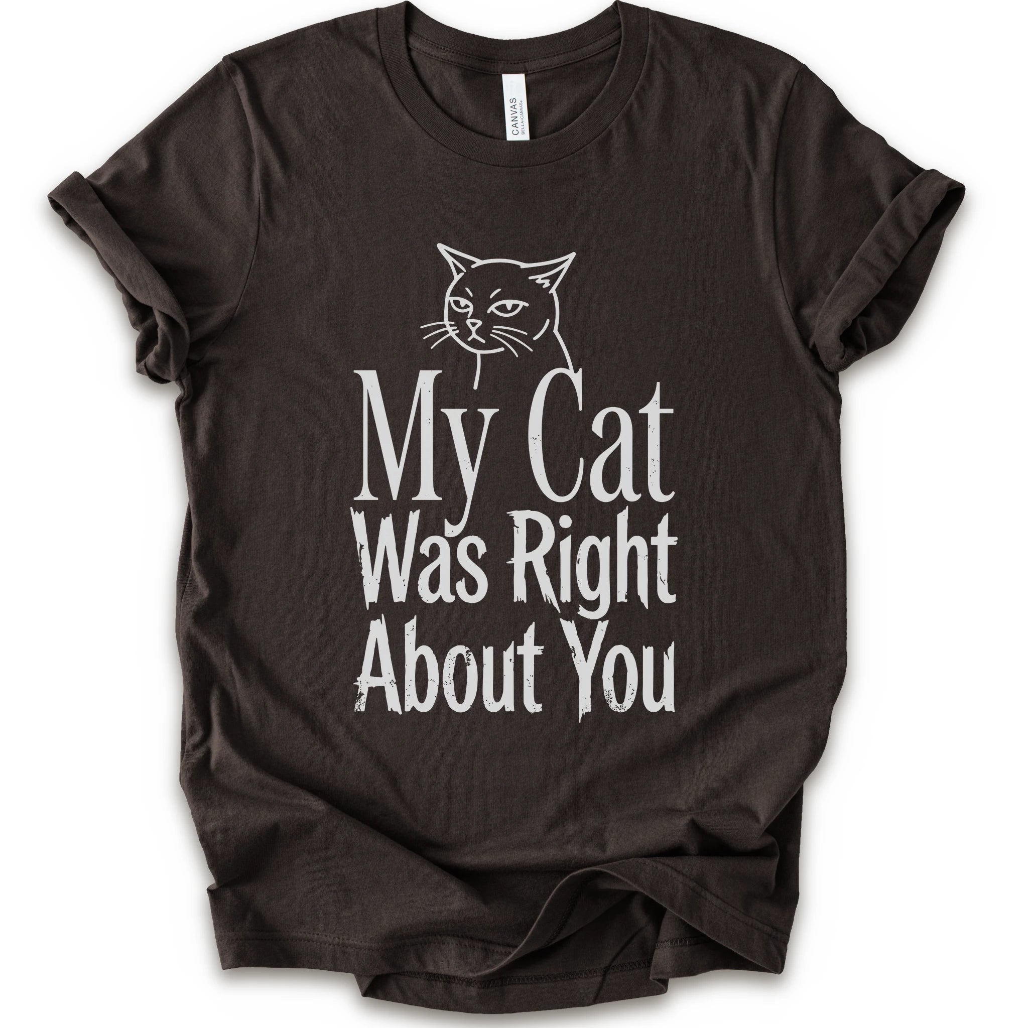 A brown short-sleeve crewneck T-shirt with a cat rendered in white outline sits above the text “My Cat Was Right About You,” arranged in oversized mixed serif and distressed lettering.