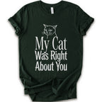 A forest short-sleeve crewneck T-shirt with a cat rendered in white outline sits above the text “My Cat Was Right About You,” arranged in oversized mixed serif and distressed lettering.