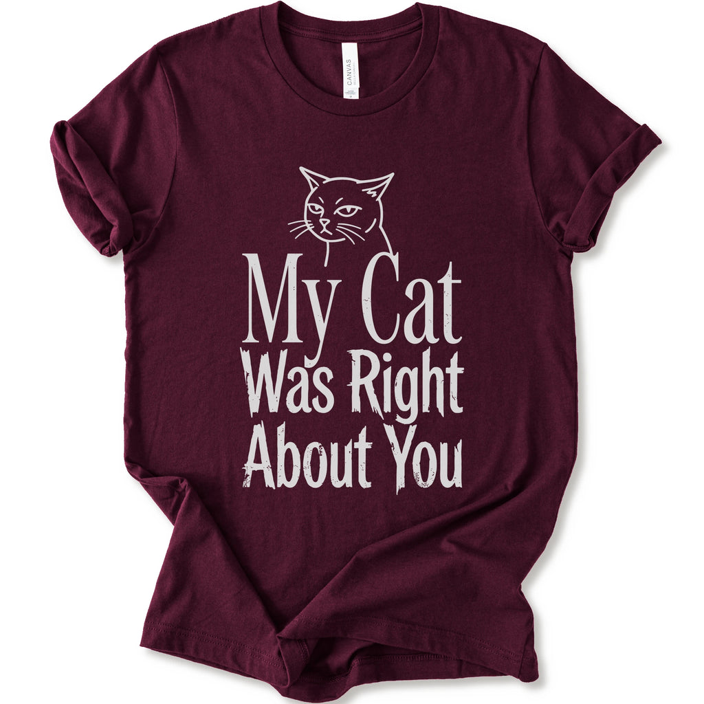 A maroon short-sleeve crewneck T-shirt with a cat rendered in white outline sits above the text “My Cat Was Right About You,” arranged in oversized mixed serif and distressed lettering.