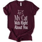 A maroon short-sleeve crewneck T-shirt with a cat rendered in white outline sits above the text “My Cat Was Right About You,” arranged in oversized mixed serif and distressed lettering.
