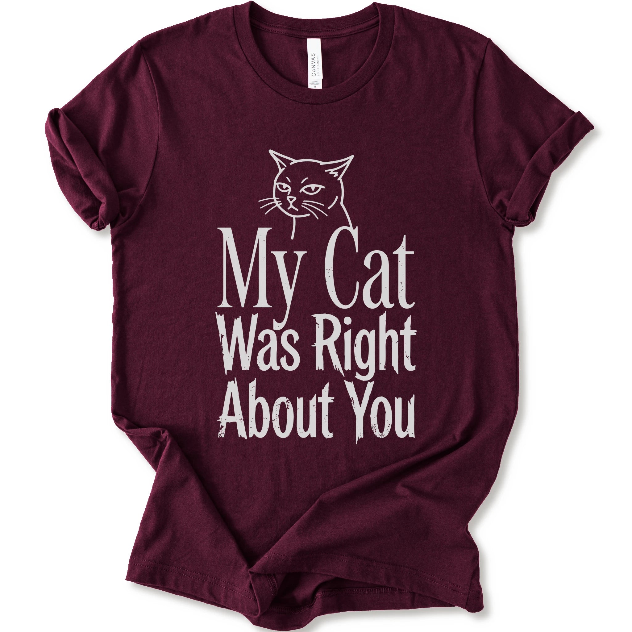 A maroon short-sleeve crewneck T-shirt with a cat rendered in white outline sits above the text “My Cat Was Right About You,” arranged in oversized mixed serif and distressed lettering.