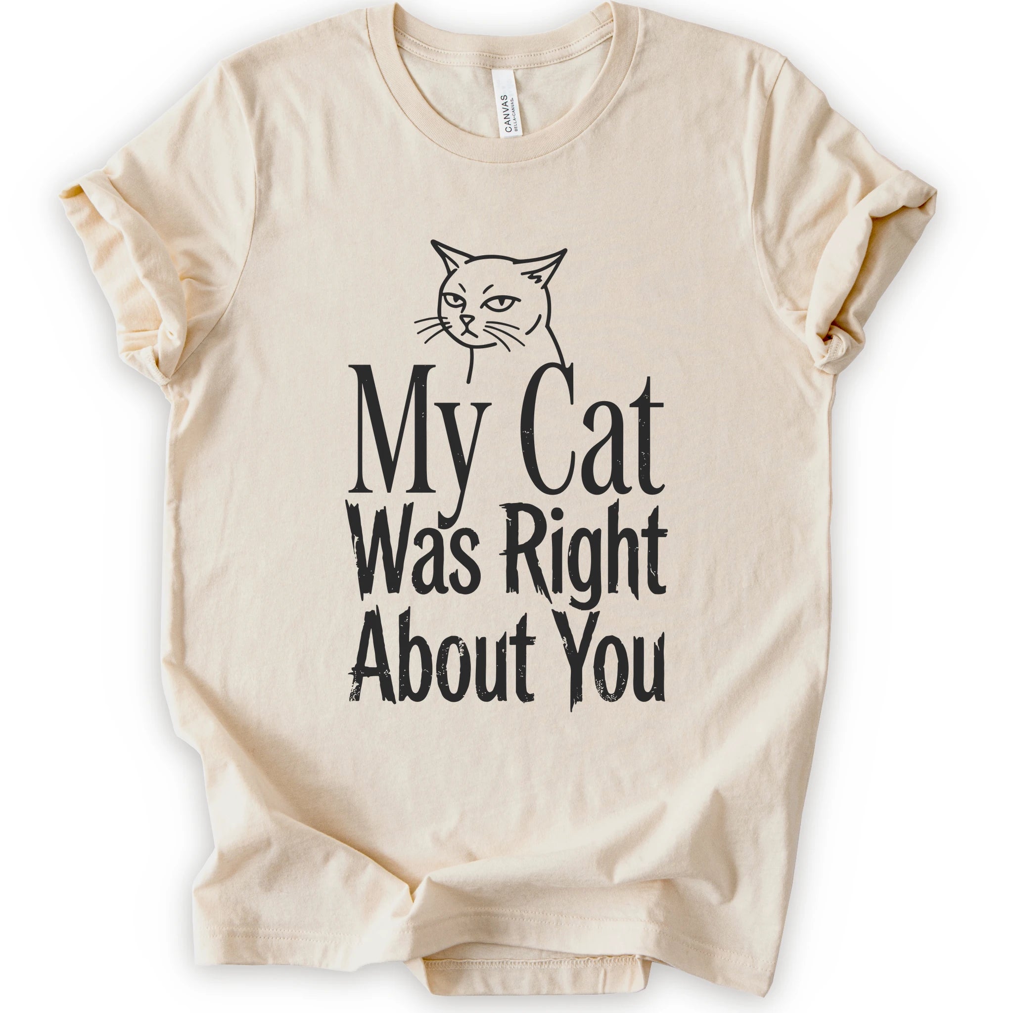 A natural short-sleeve crewneck T-shirt with a cat rendered in black outline sits above the text “My Cat Was Right About You,” arranged in oversized mixed serif and distressed lettering.