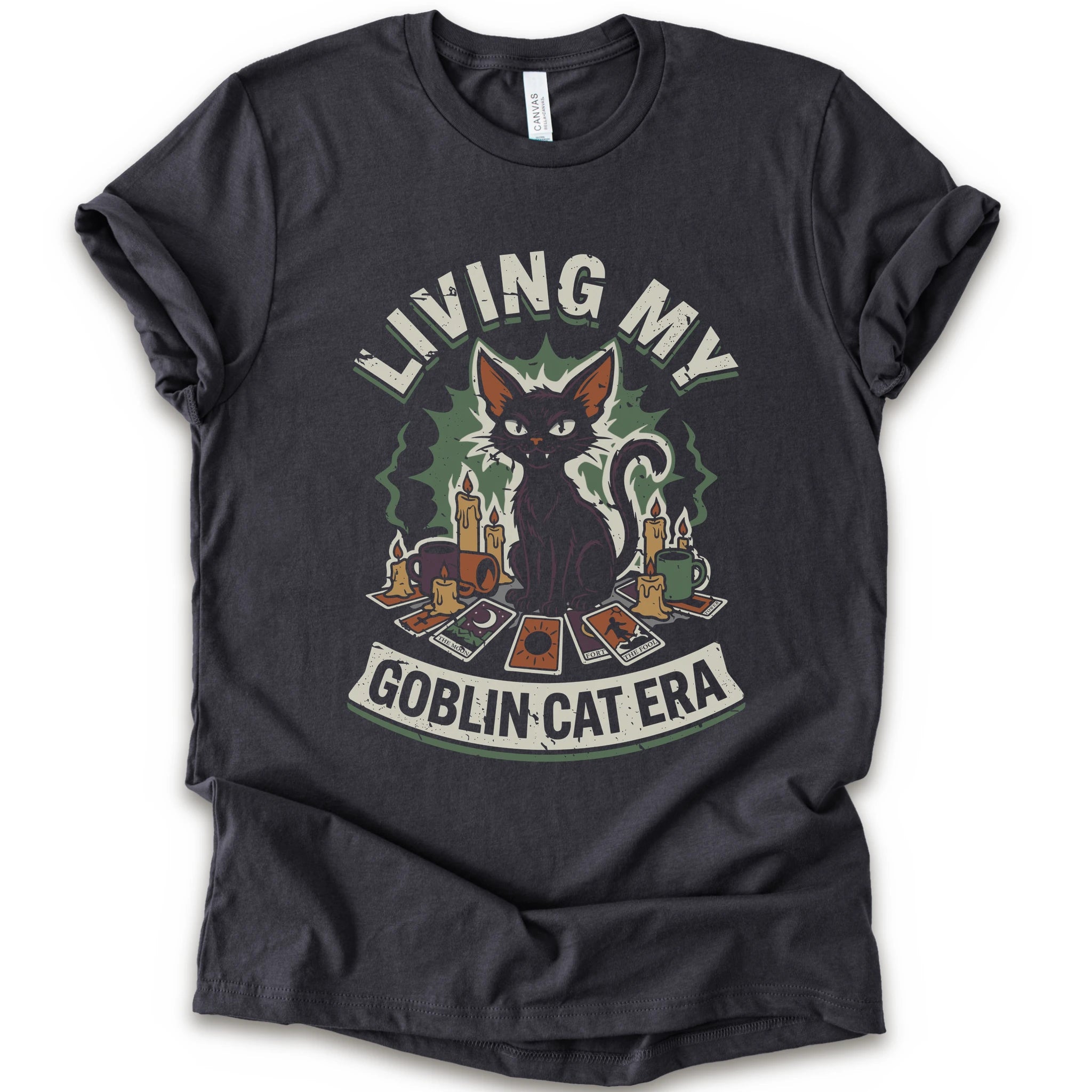 A dark grey short-sleeve t-shirt with a graphic print of a black cat surrounded by candles, cards, and the text 'LIVING MY GOBLIN CAT ERA' in a distressed vintage style.
