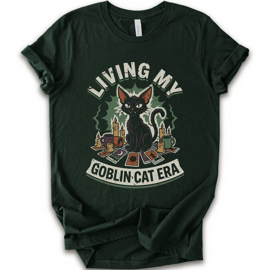 A forest short-sleeve t-shirt with a graphic print of a black cat surrounded by candles, cards, and the text 'LIVING MY GOBLIN CAT ERA' in a distressed vintage style.