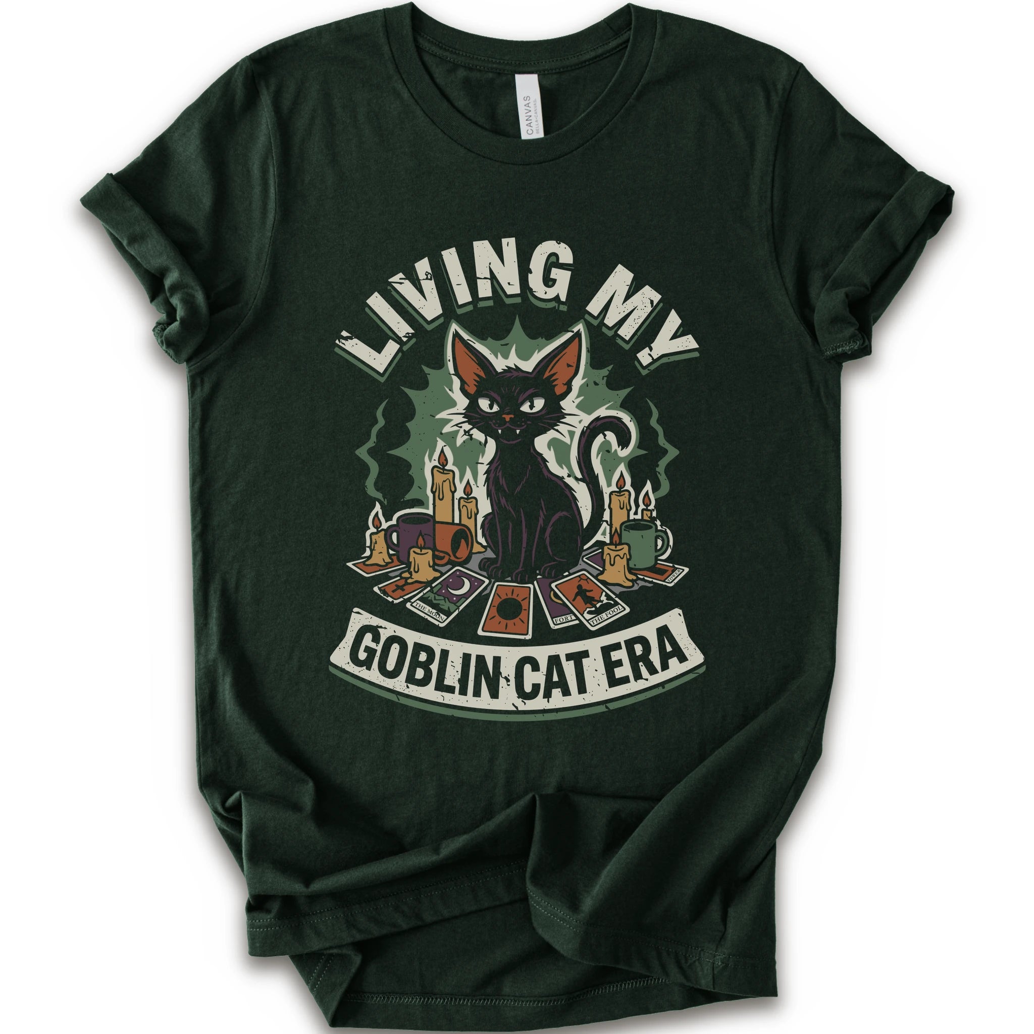 A forest short-sleeve t-shirt with a graphic print of a black cat surrounded by candles, cards, and the text 'LIVING MY GOBLIN CAT ERA' in a distressed vintage style.