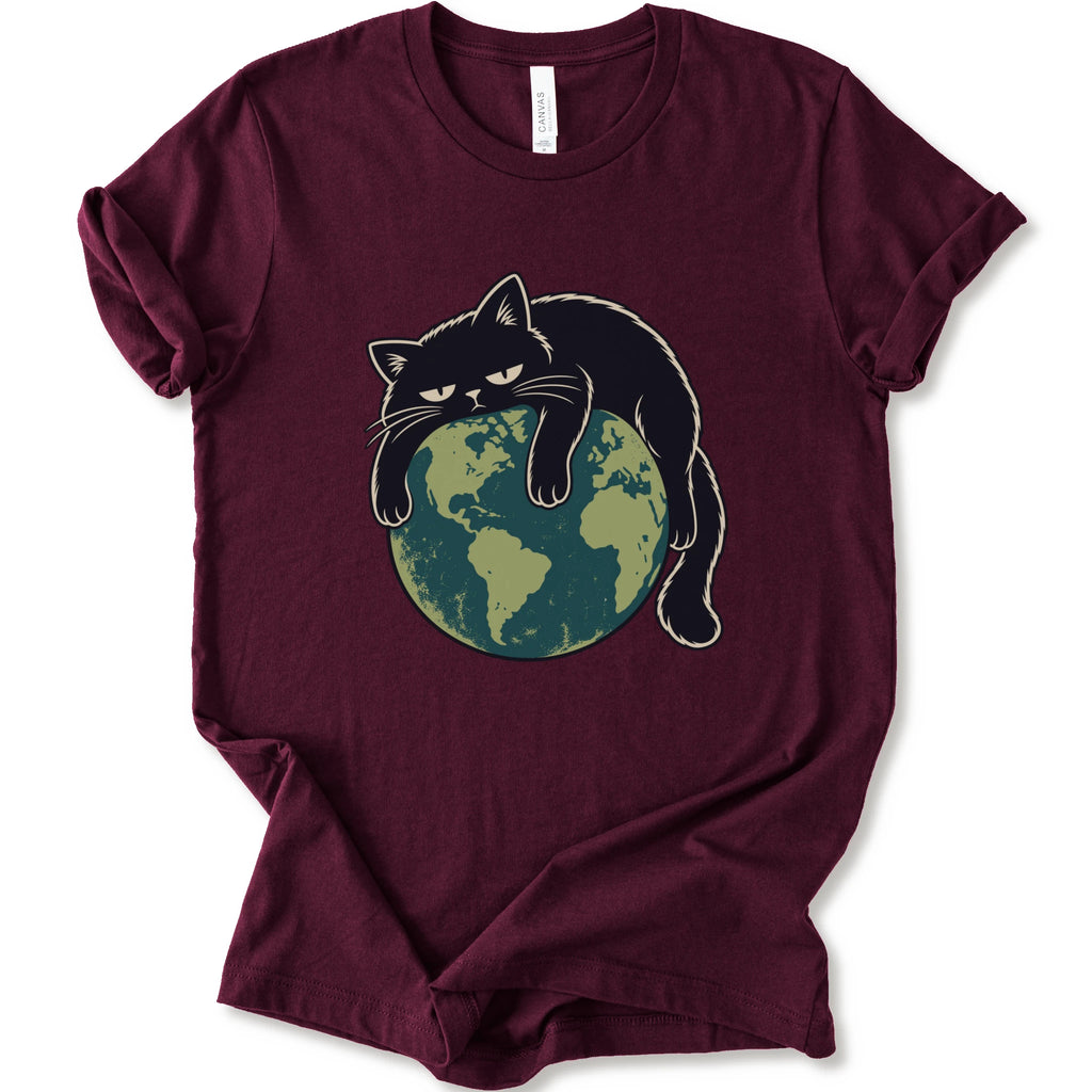 A maroon short-sleeve crewneck t-shirt featuring a graphic of a grumpy black cat draped over a green and blue globe.