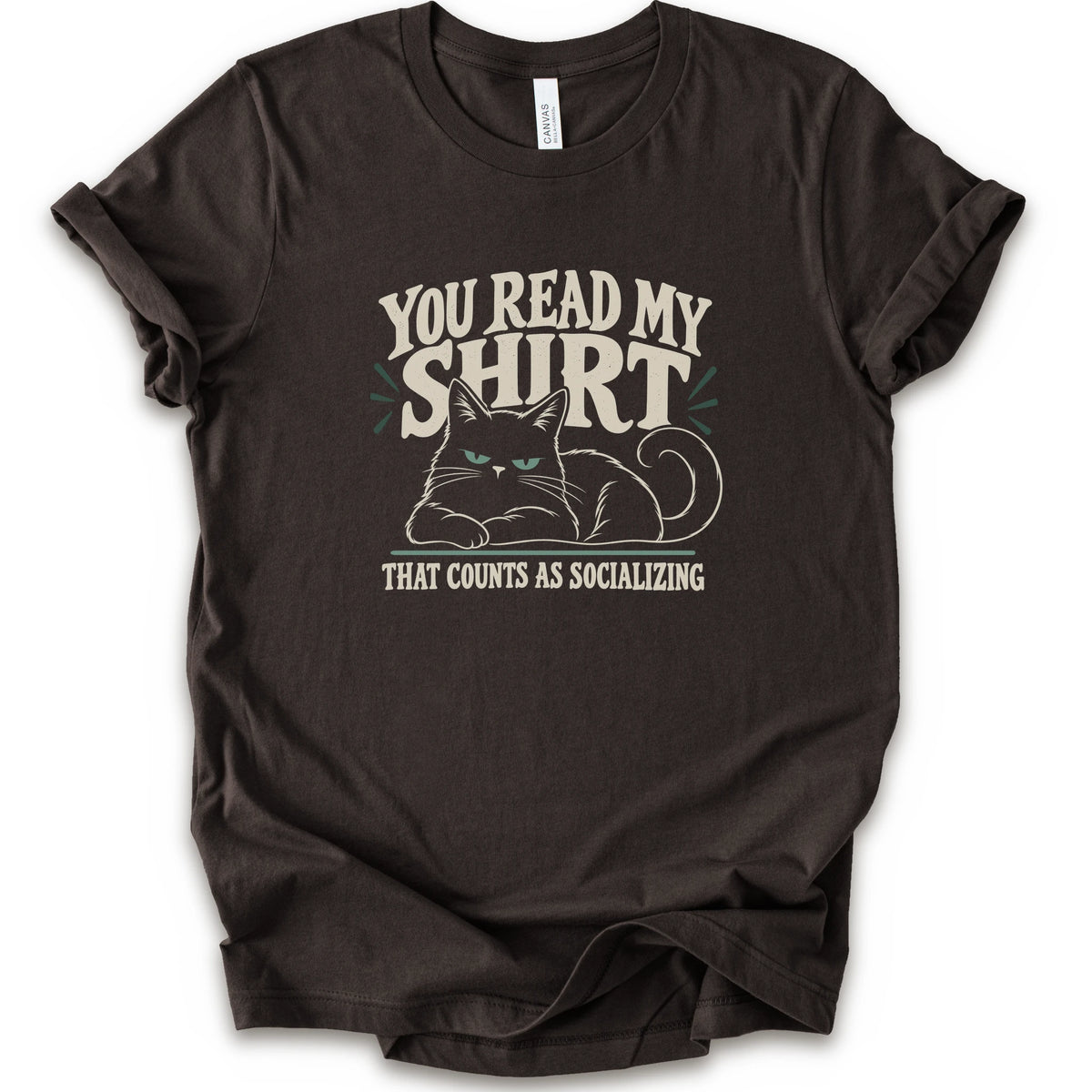 A brown short-sleeve crewneck t-shirt with a graphic print of a grumpy cat and the text 'YOU READ MY SHIRT THAT COUNTS AS SOCIALIZING' in cream and light green.