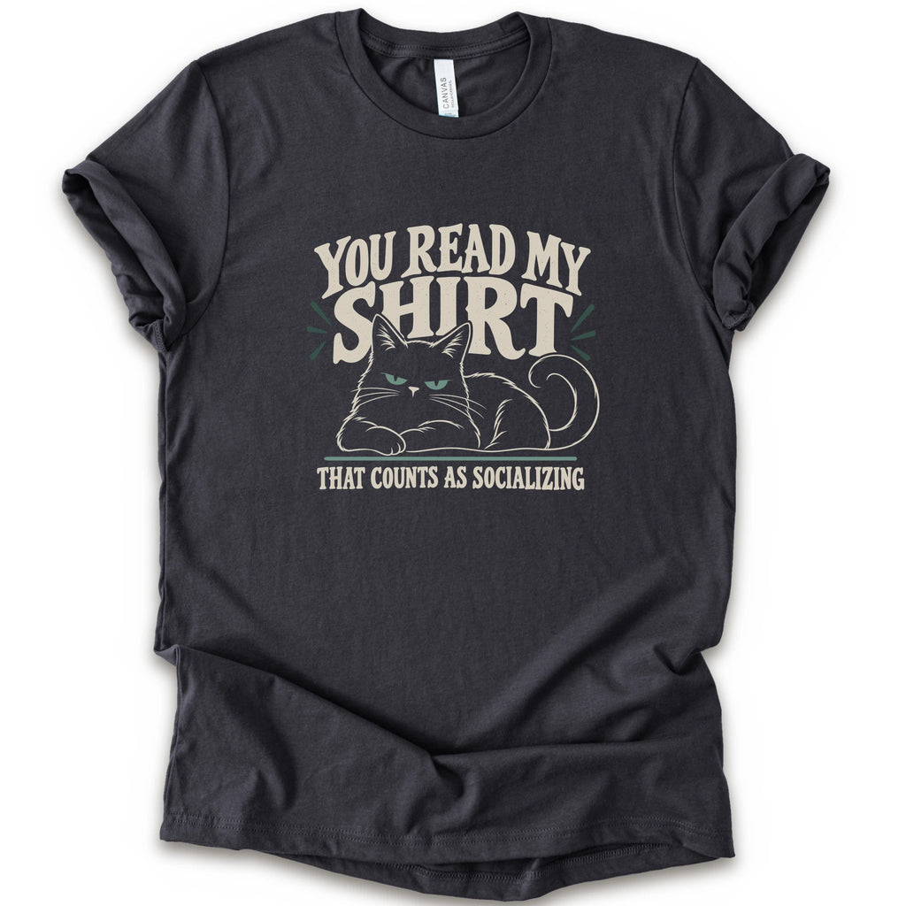A dark grey short-sleeve crewneck t-shirt with a graphic print of a grumpy cat and the text 'YOU READ MY SHIRT THAT COUNTS AS SOCIALIZING' in cream and light green.