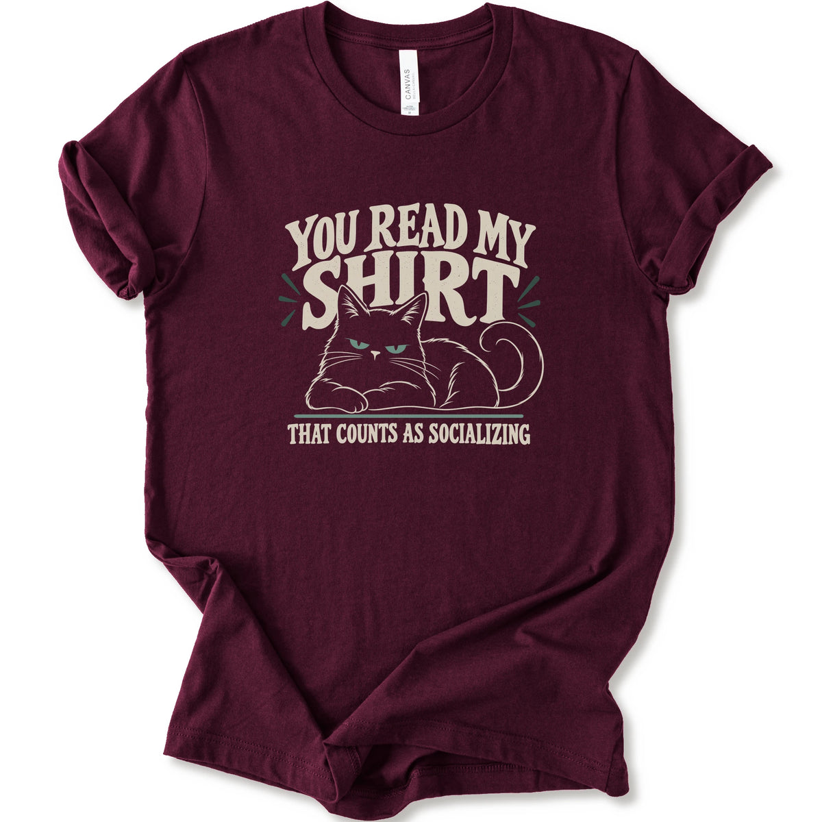 A maroon short-sleeve crewneck t-shirt with a graphic print of a grumpy cat and the text 'YOU READ MY SHIRT THAT COUNTS AS SOCIALIZING' in cream and light green.