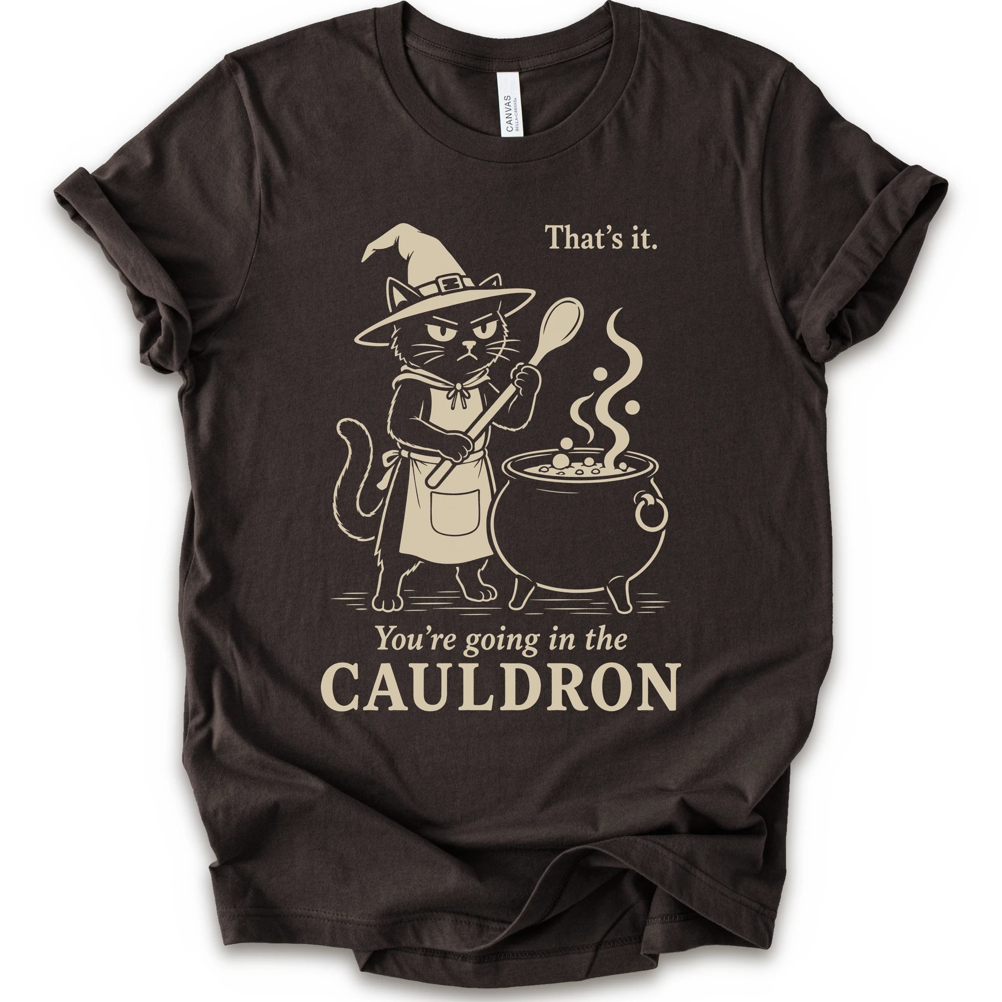 Brown graphic t-shirt with cat as a witch stirring a bubbling cauldron with “That’s it, you’re going in the cauldron” text