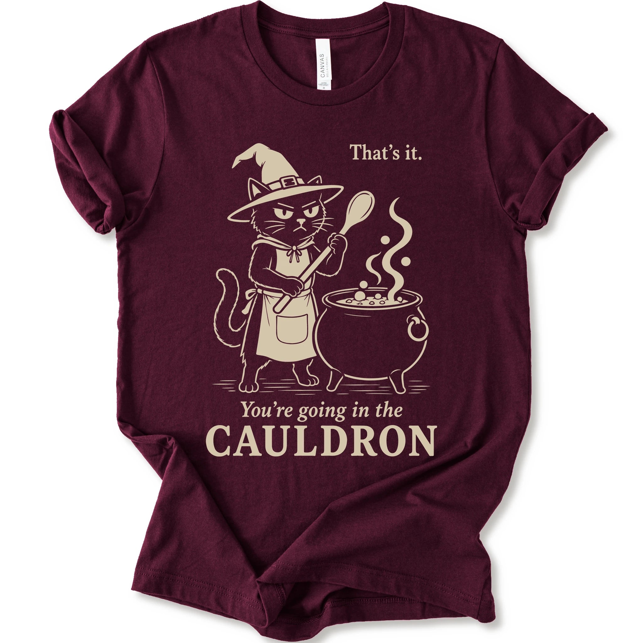 Maroon graphic t-shirt with cat as a witch stirring a bubbling cauldron with “That’s it, you’re going in the cauldron” text